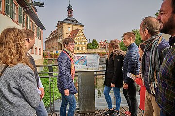 Eine Stadtführungsgruppe steht auf dem Ochsenklaviersteg an einer Tafel des Flusspfades entlang der Regnitz. Im Hintergurnd ist das Alte Rathaus.