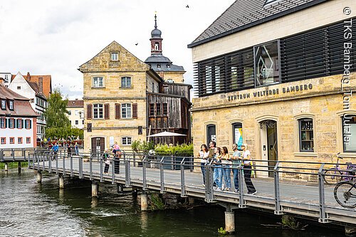 Eine Gruppe Touristen steht auf der Brücke vor dem Zentrum Welterbe Bamberg.